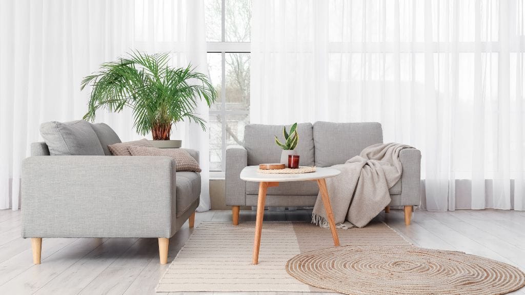 Salón con sofá minimalista y gran ventanal con cortinas blancas.